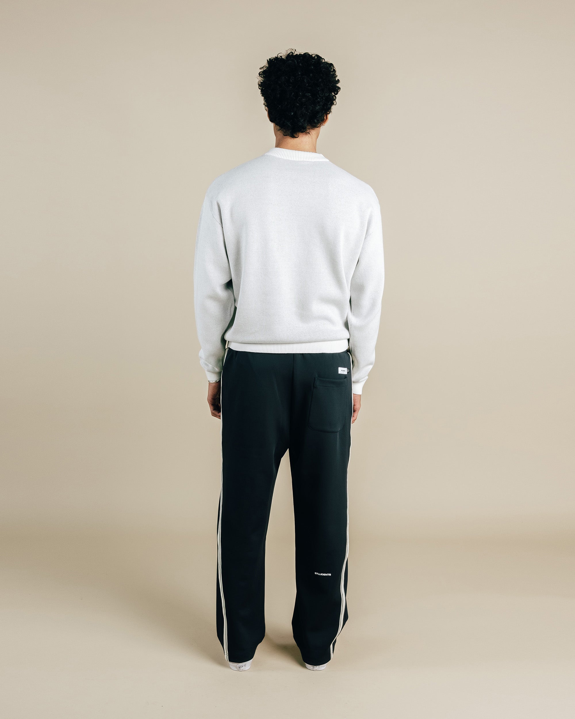 Person wearing a light gray sweatshirt and black pants with white stripes on a beige background