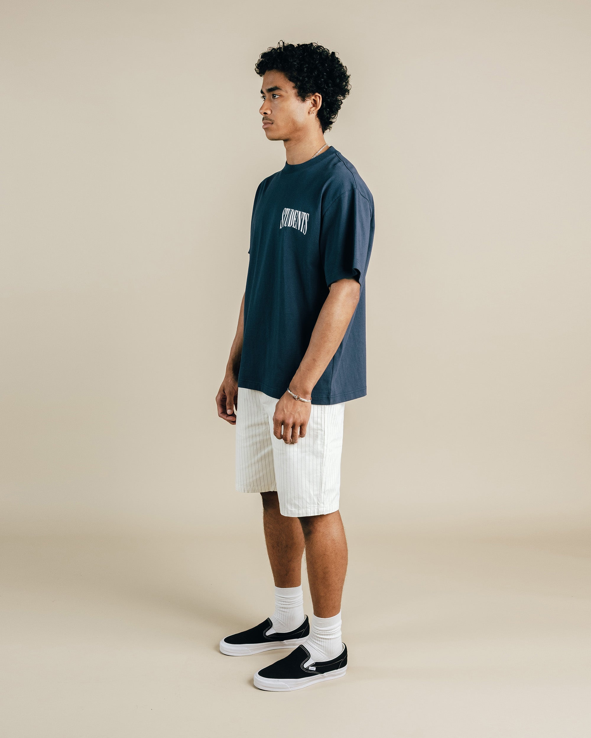 Person wearing a dark blue t-shirt with text, white shorts, and black sneakers on a beige background