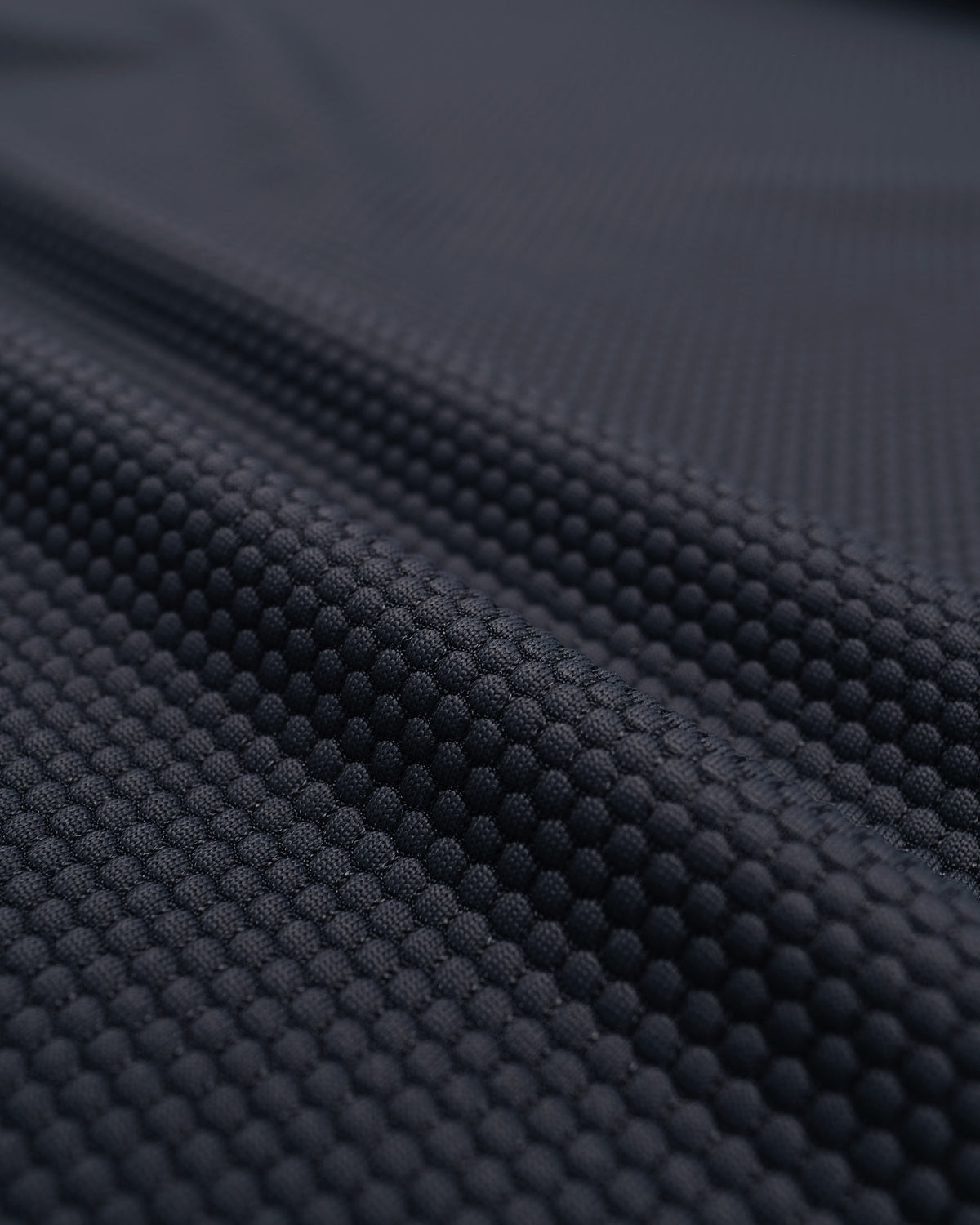 Close-up of a dark navy textured fabric with a raised dotted or honeycomb-like pattern, shown in soft folds.